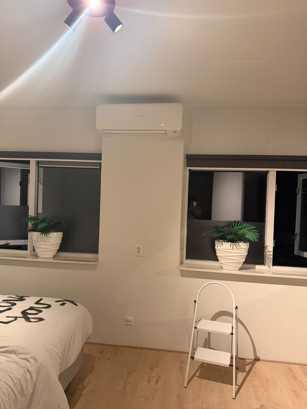 Witte airco binnenunit tussen twee ramen in een slaapkamer